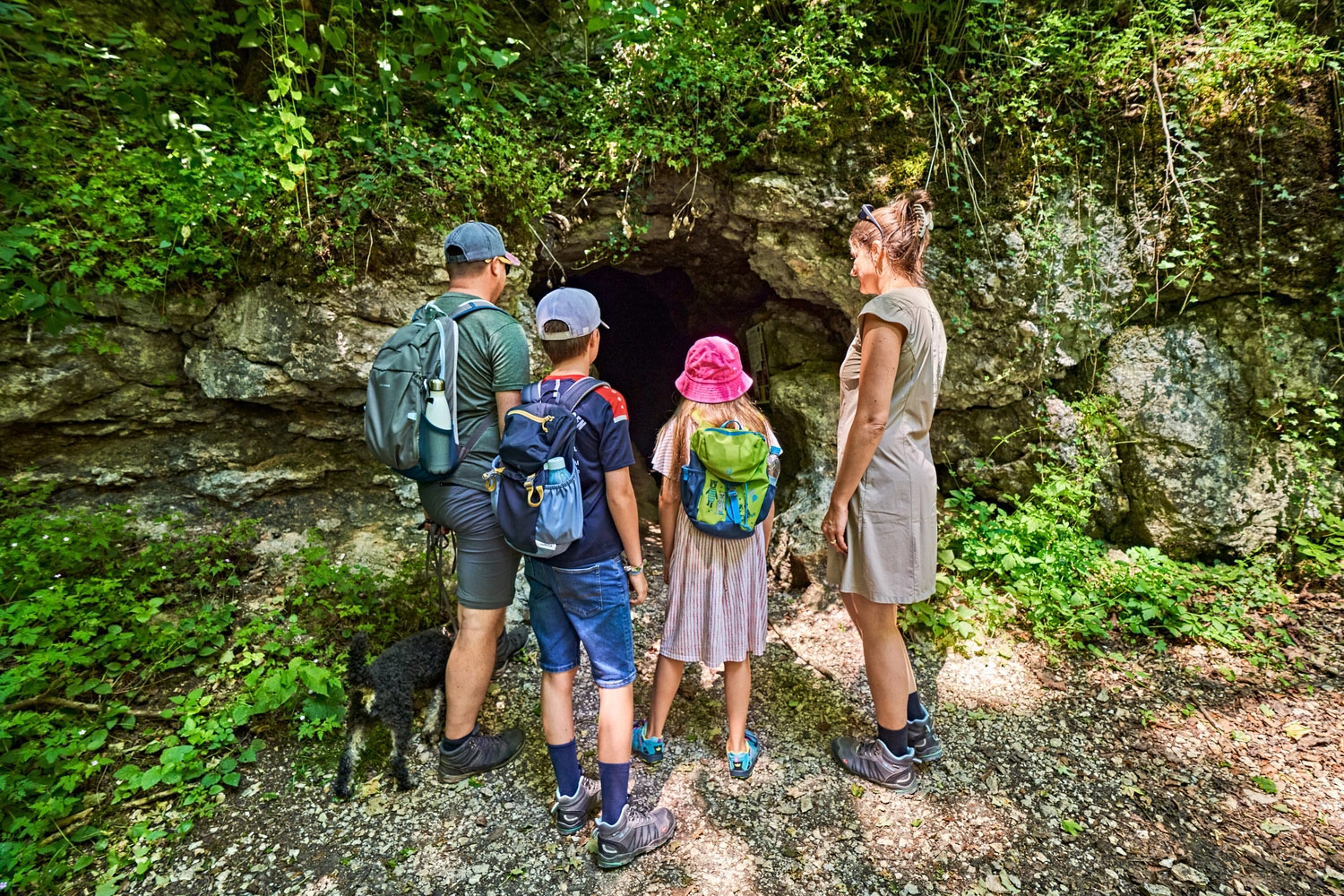 Familie mit zwei Kindern und Hund steht vor dem Eingang einer Felsenhöhle im Grünen auf der Schwäbischen Alb.