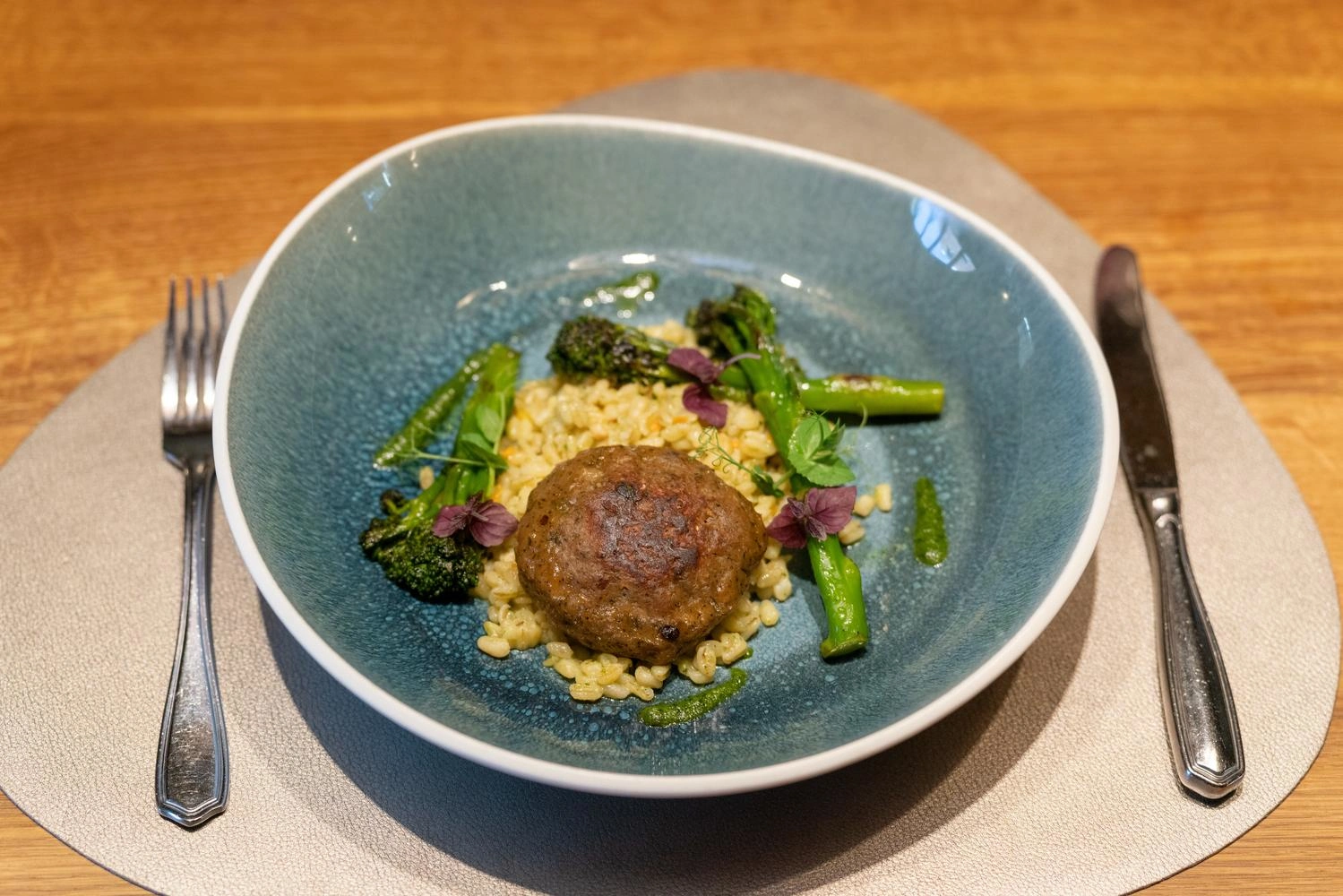  Vegan boulette with wheat risotto, broccoli and pesto served on a deep blue plate.