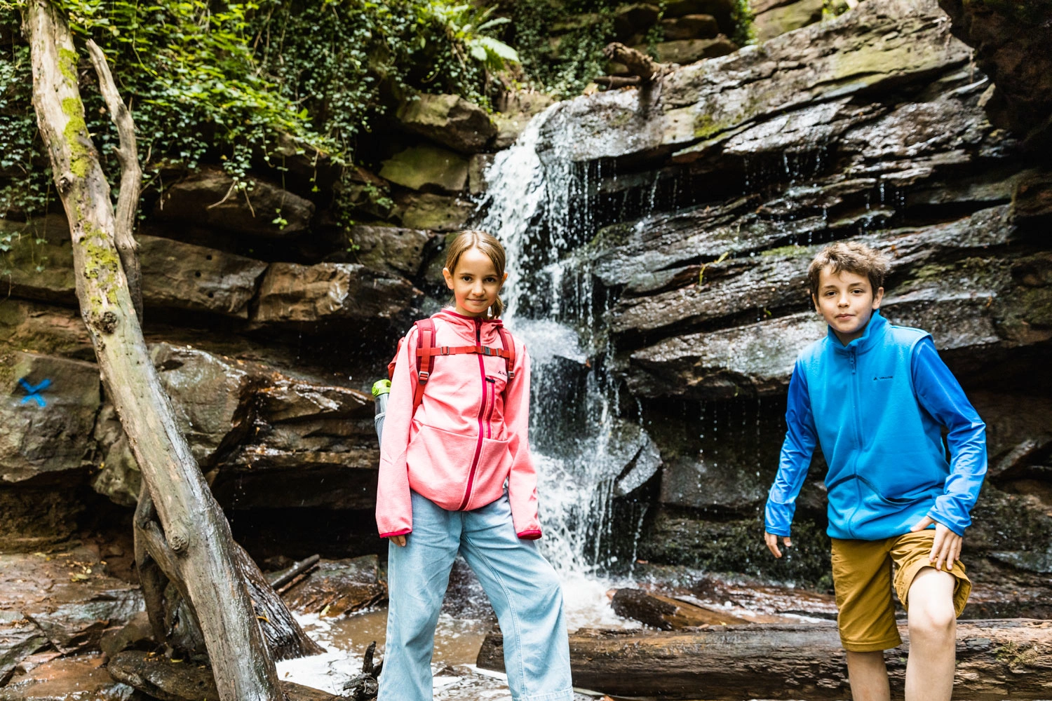 Ein Junge und ein Mädchen stehen vor einem Wasserfall in einer Schlucht.