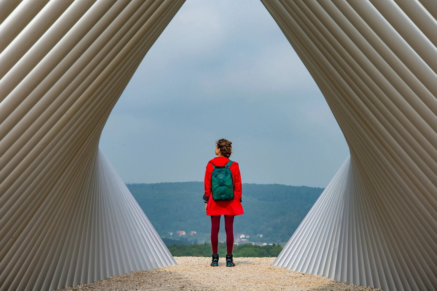  A person in a red jacket stands under a large metal sculpture and enjoys the view.