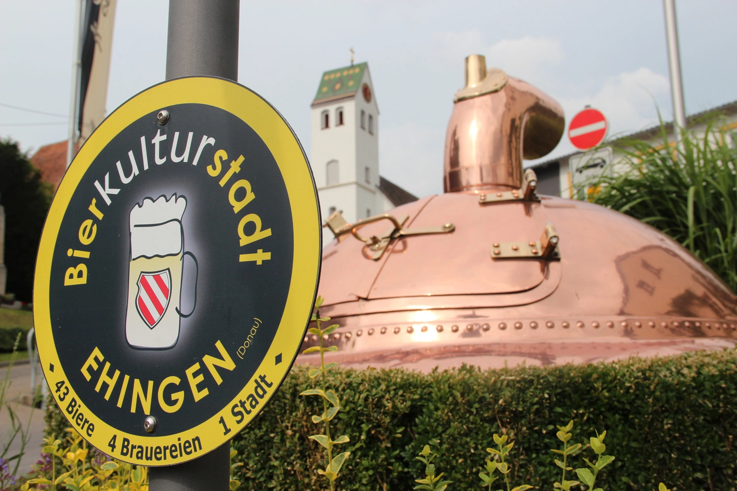 Giant brewing kettle and a town sign with beer mug in front of a town entrance
