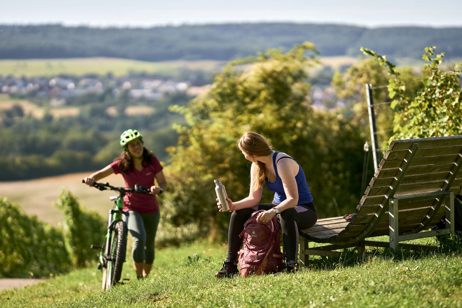 Person mit Fahrrad und Person auf einer Bank mit Rucksack bei einer Pause auf einem Aussichtspunkt im Taubertal.