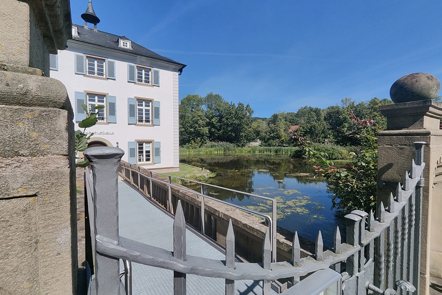 View over a fence to a small lake and the castle. The sky is bright blue.