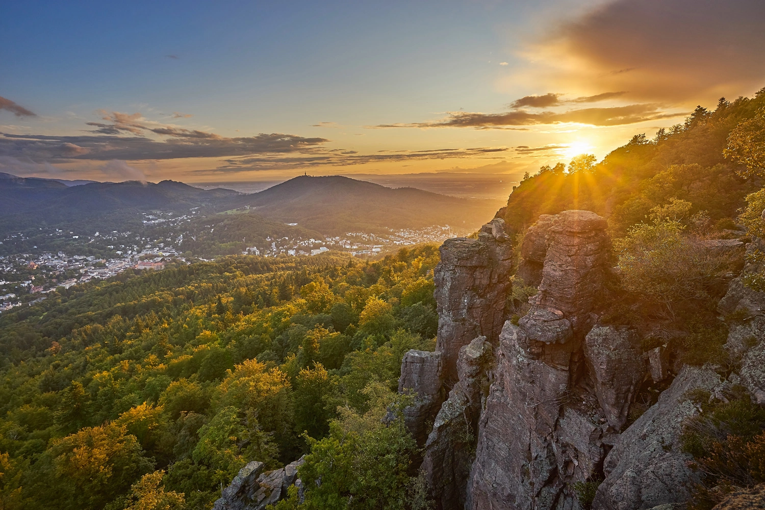 Sunset at the Battert Cliffs near Baden-Baden: a view across forested hills and the valley, with striking rock formations bathed in the warm evening light.