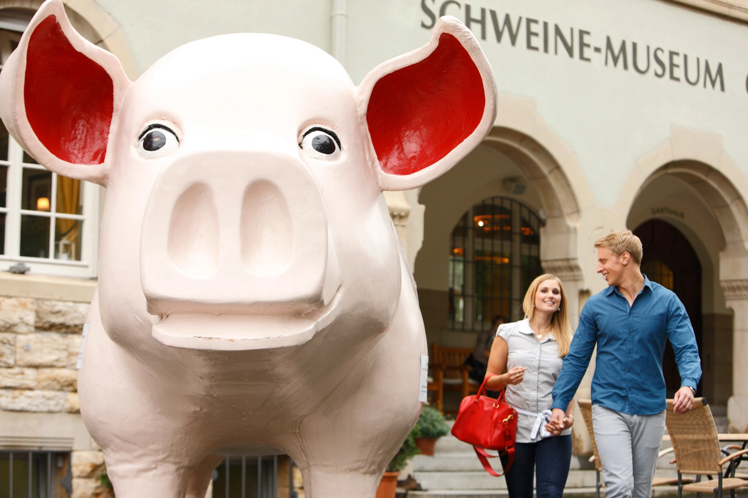 Ein Pärchen neben einem riesigen Schweine-Modell vor dem Eingang eines Museums