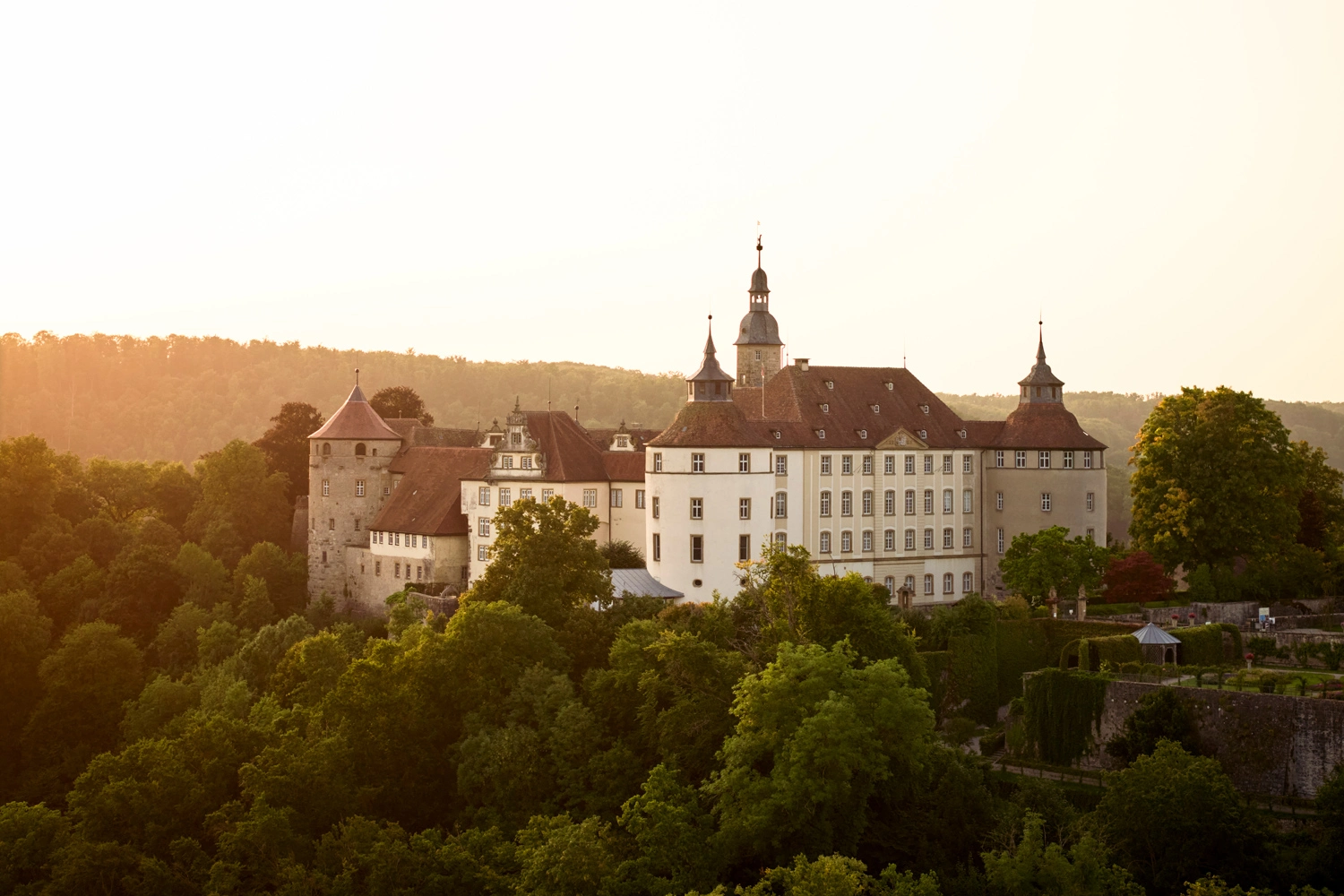 Langenburg Castle in Hohenlohe, surrounded by green trees, sits enthroned on a hill in the warm light of the evening sun.