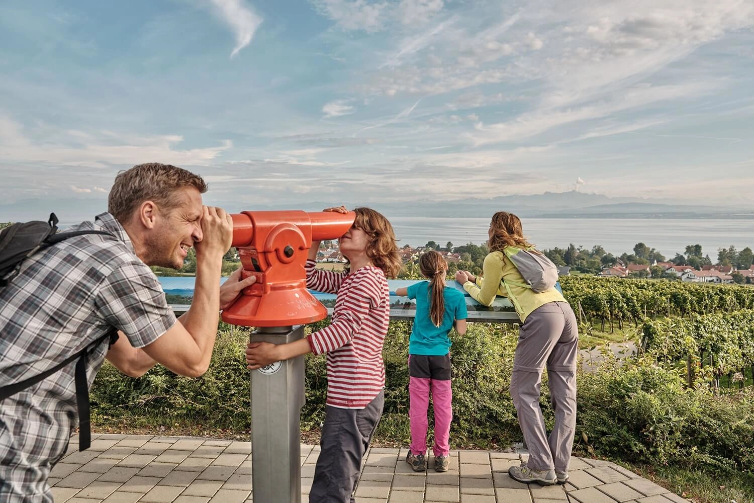 A family at a lookout point overlooking Lake Constance, using a telescope.