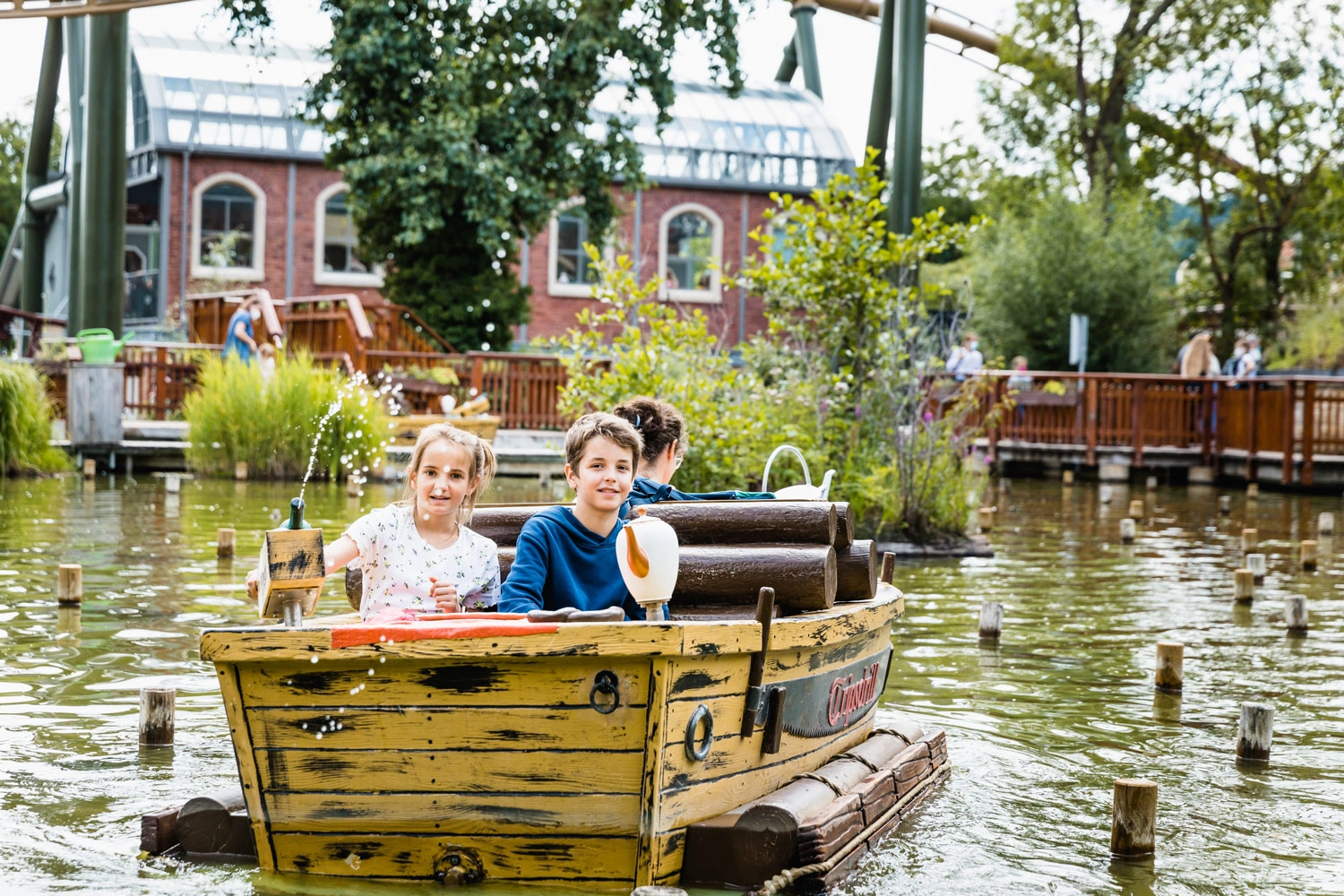 Ein Junge und ein Mädchen sitzen in einen kleinen Boot auf einem Teich in einem Freizeitpark und spritzen mit einer Wasserpistole.