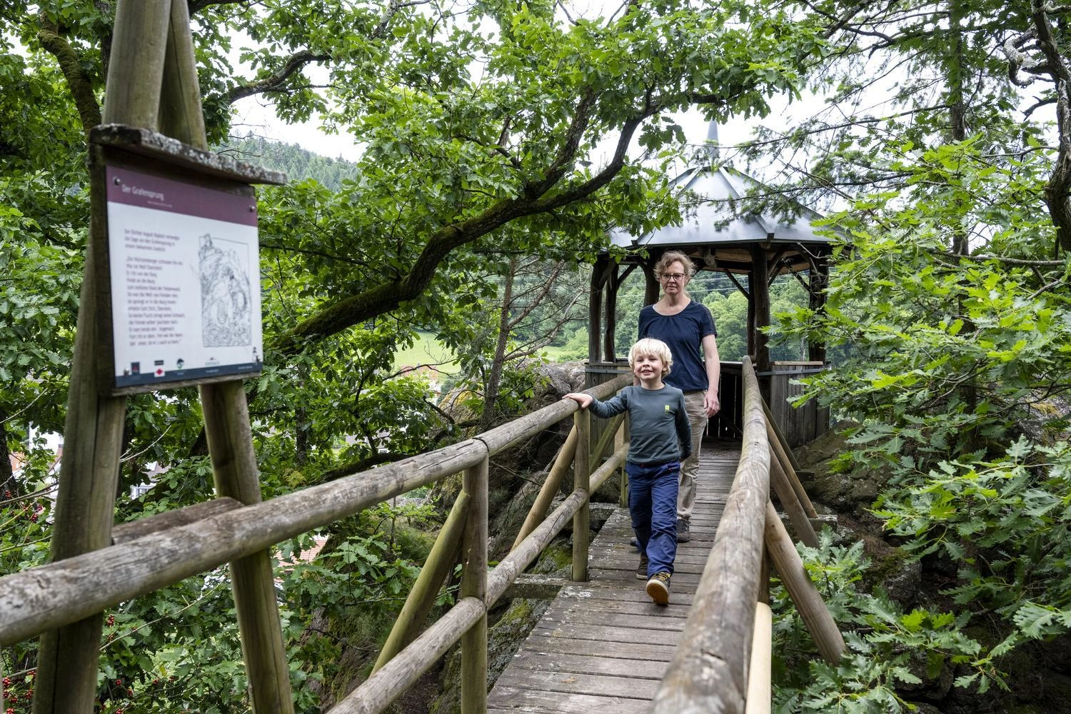 Holzbrücke führt durch dichtes Grün zu einem Pavillon, mit Infotafel zum Grafensprung am Gernsbacher Sagenweg.