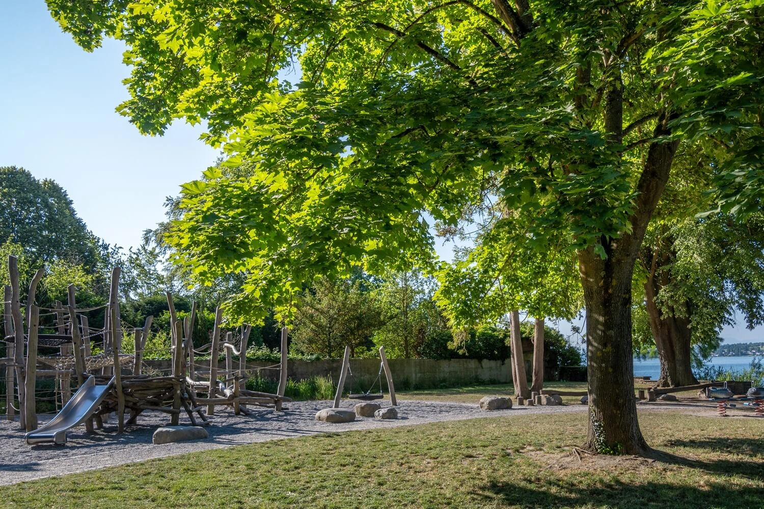 A playground surrounded by trees, with a lake in the background.
