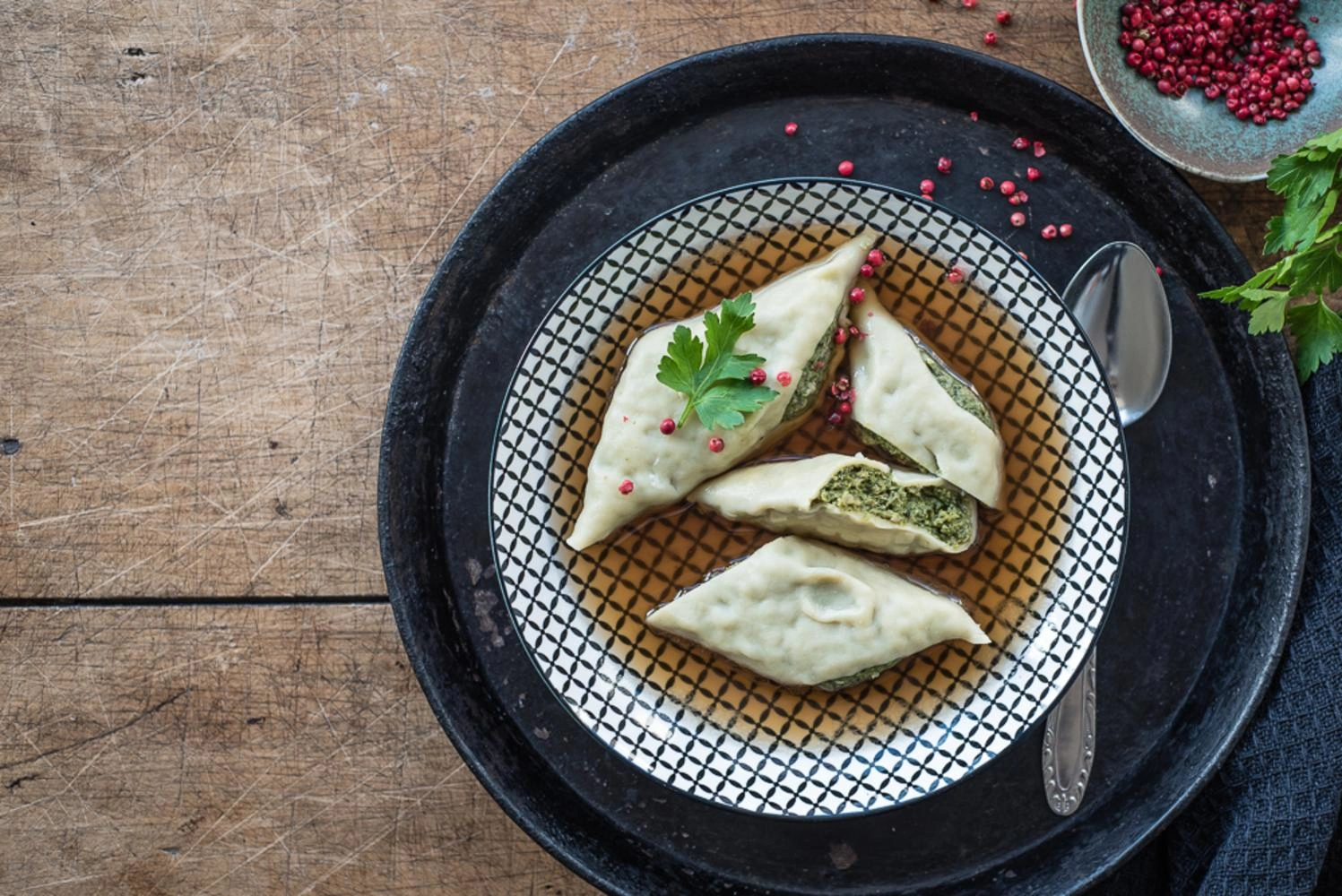 Top view of a plate with four Maultaschen in the broth on a rustic wooden table.