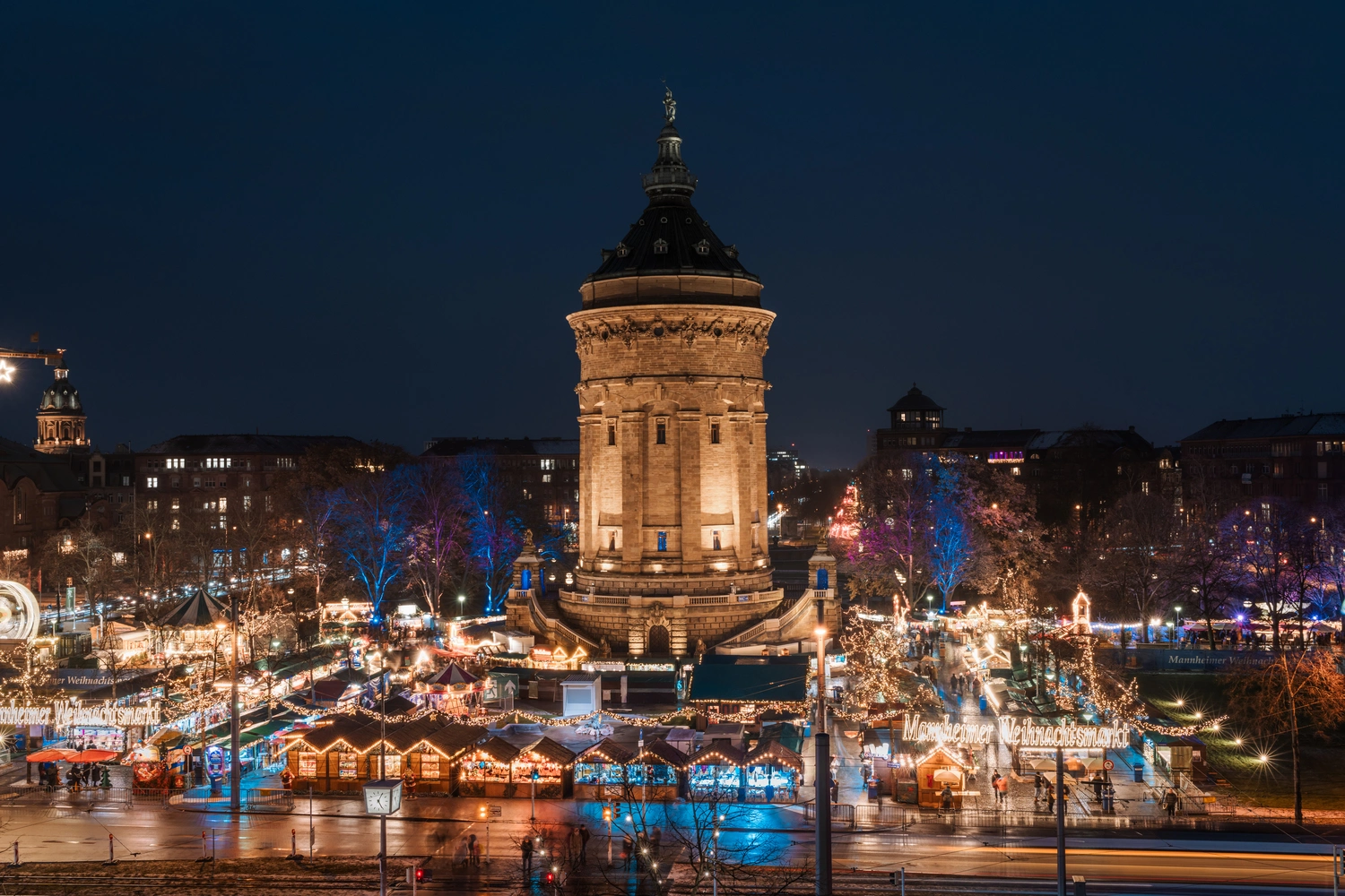 An illuminated Christmas market is set up around a tower.