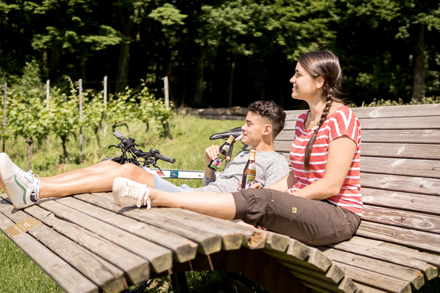 A couple relaxes on a wooden lounger and drinks a beer.