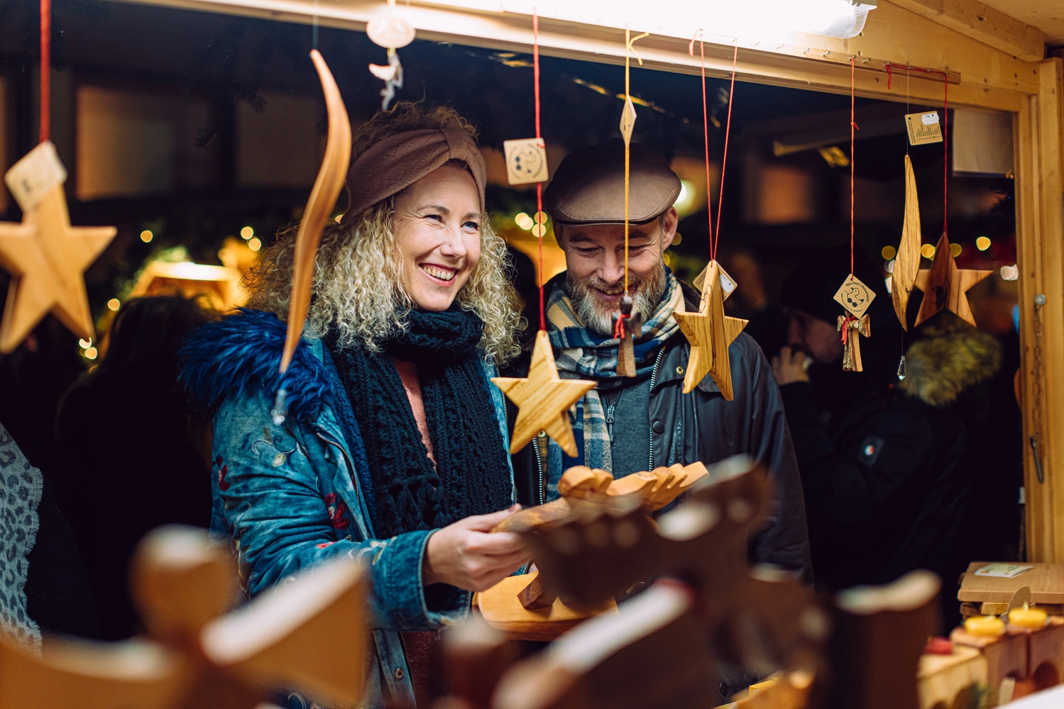 Eine Frau und ein Mann stehen an einem Weihnachtsmarktstand und schauen Holzdekoration an.