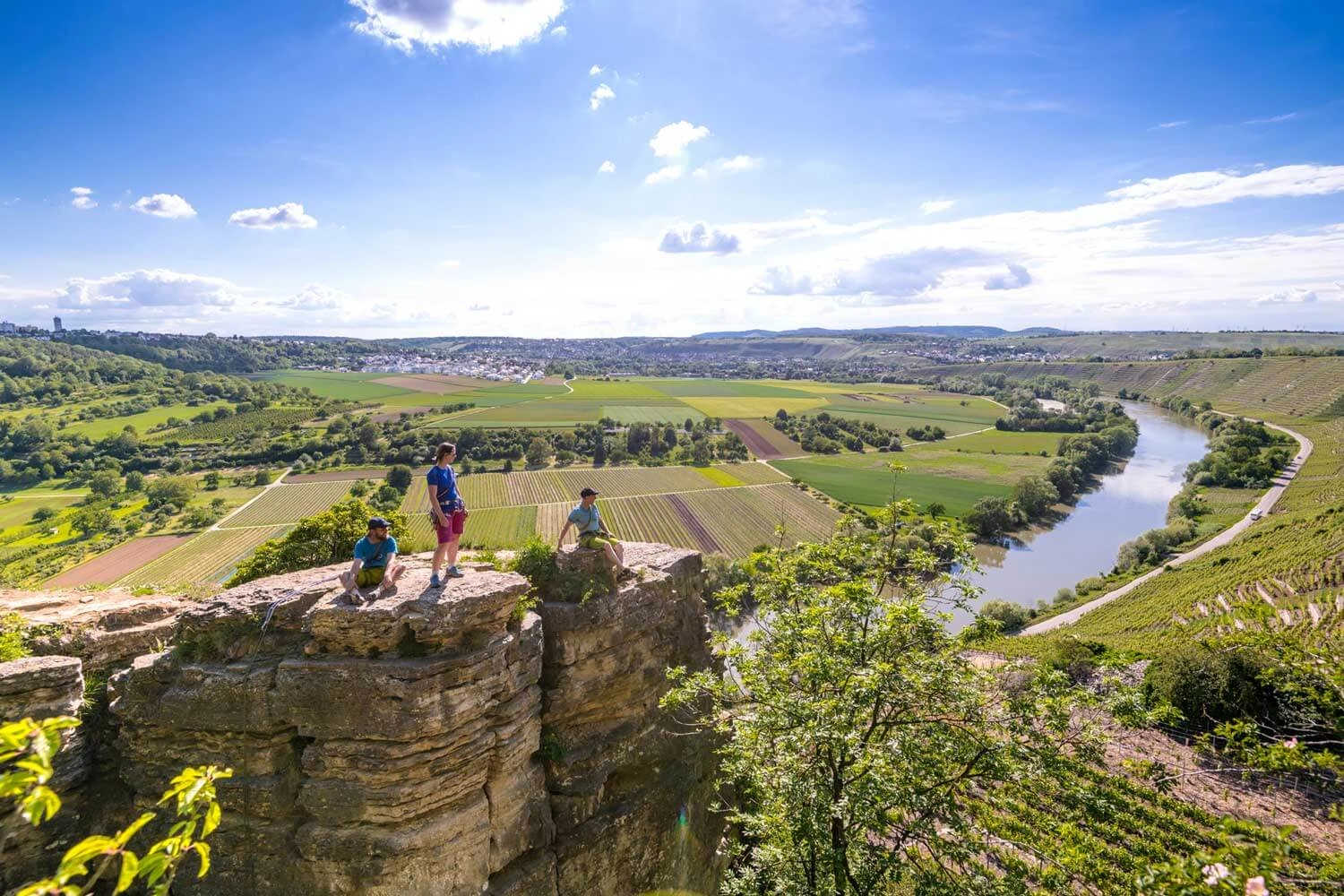 Climbers stand on a rock and enjoy the view. A river flows in the background.