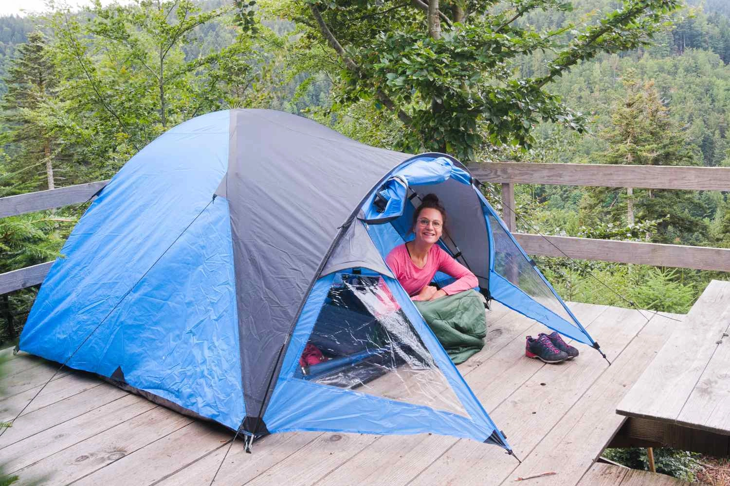 A woman is sitting in her tent on a wooden platform at a small campground in the middle of the forest.