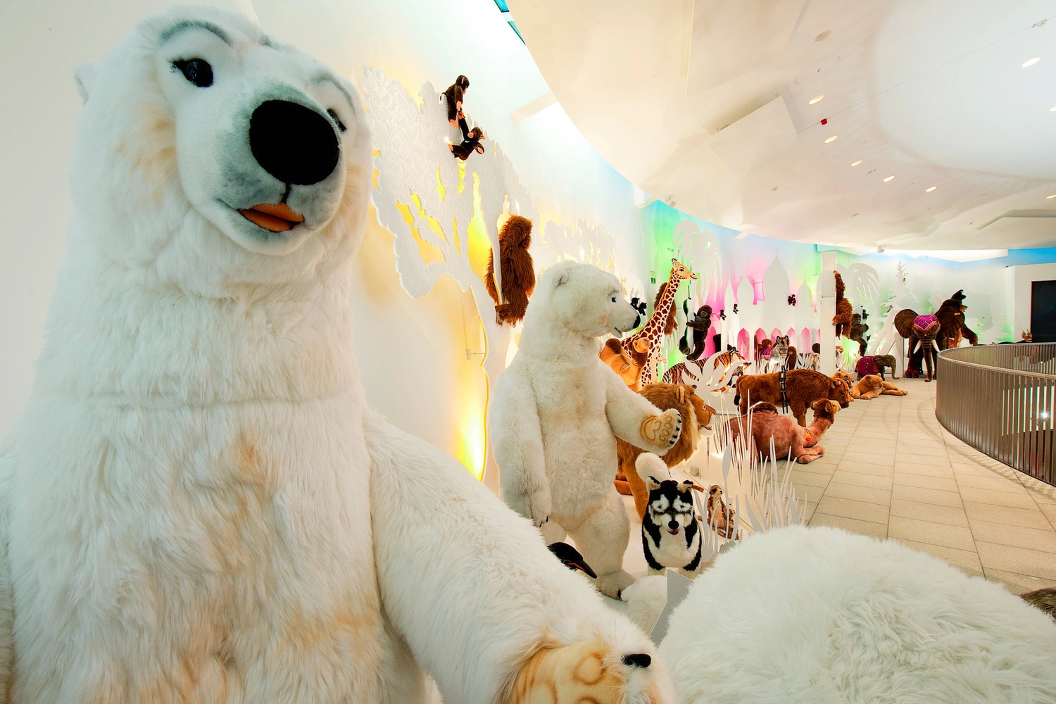 Ausstellung mit großen Plüschtieren, darunter Eisbären, Pinguine und weitere Tiere, vor einer farbig beleuchteten Wand im Museum.