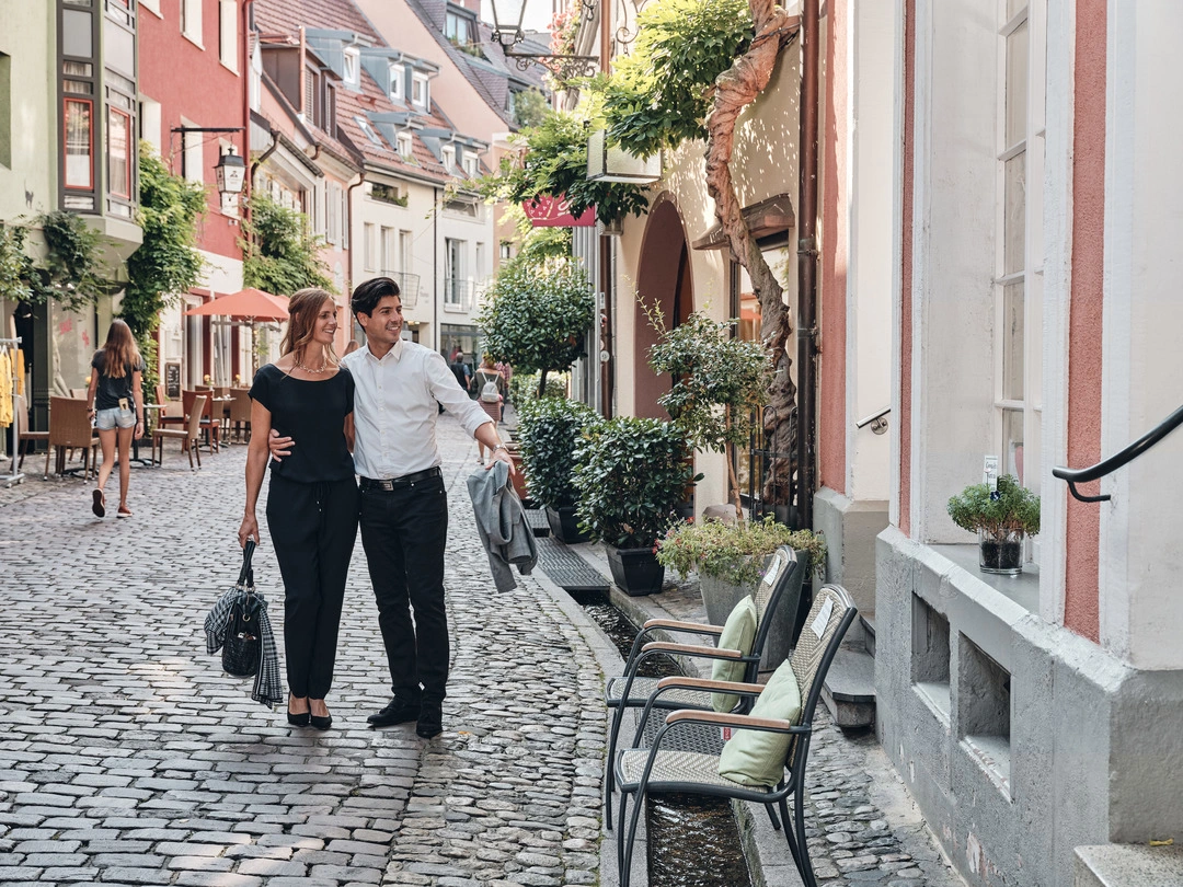 A smartly dressed couple walk arm in arm through Freiburg's old town.
