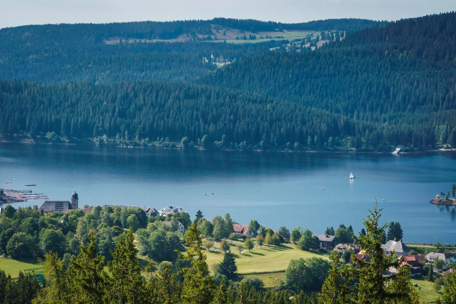 Blick auf einen See, der von bewaldeten Hügeln umgeben ist.