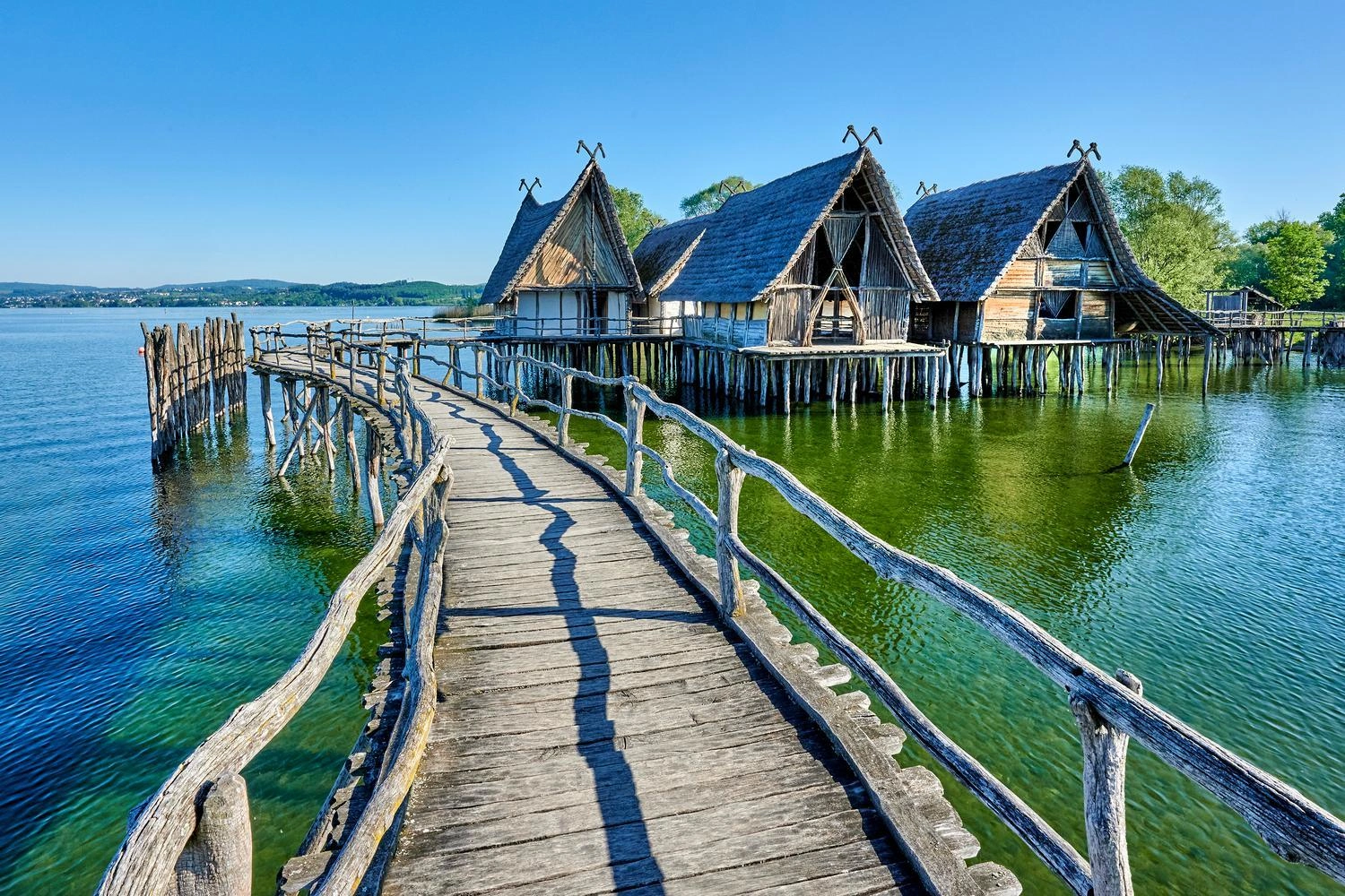 An accumulation of pile dwellings stands in a lake and can be reached via a wooden footbridge.