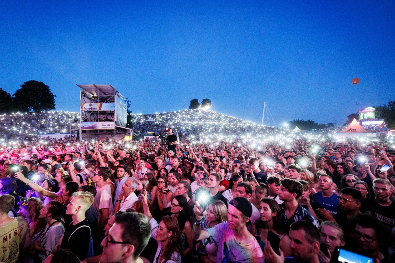 A large crowd at a festival is flashing cell phone cameras.