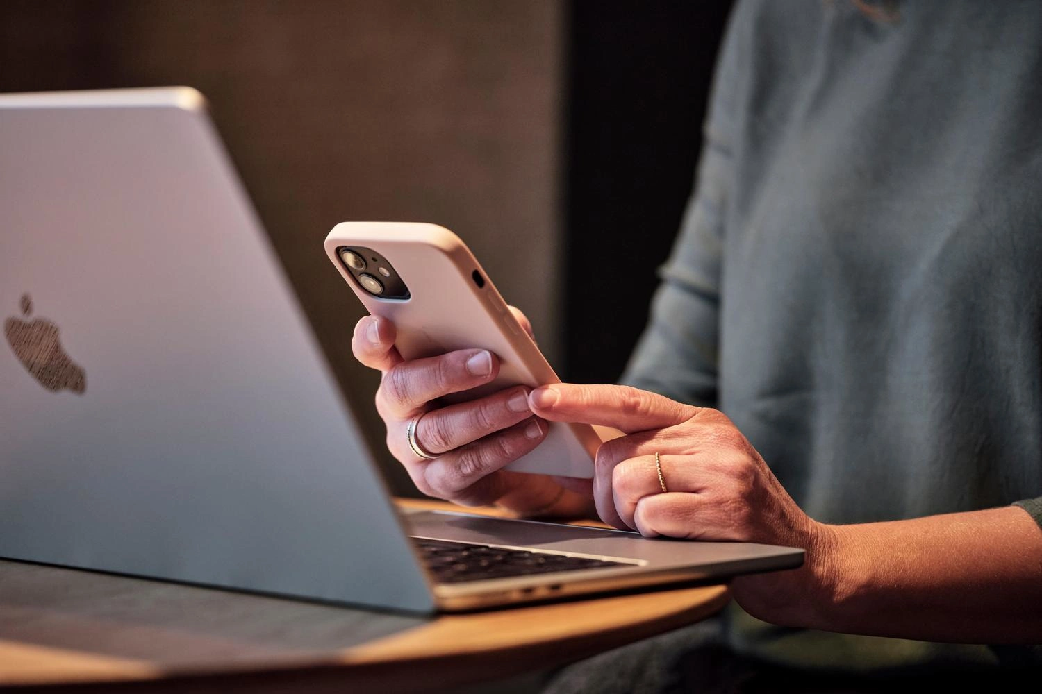 Eine Person sitzt mit einem Handy in der Hand am Laptop.