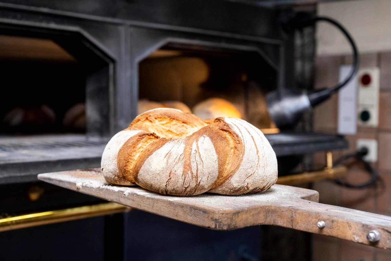 Ein frisch gebackenes Brot wird auf einem Holzbrett aus dem Ofen geholt.