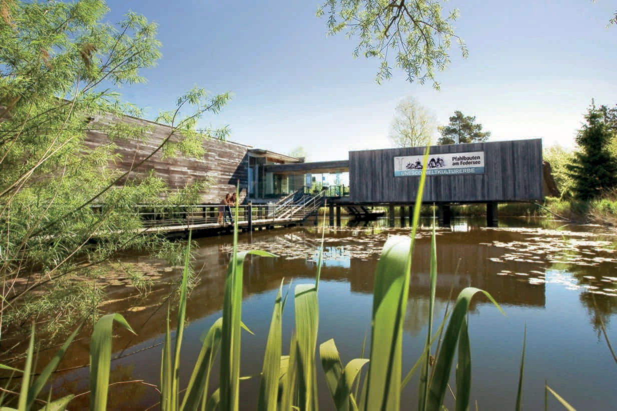 A hall-like wooden building stands on stilts in a moor.