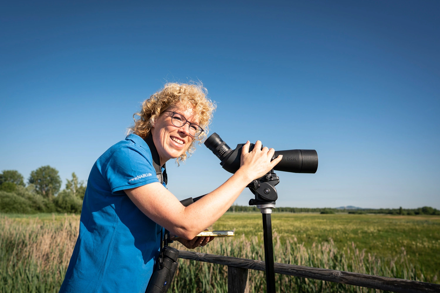 A woman stands in front of binoculars and looks out over the landscape of Federsee.