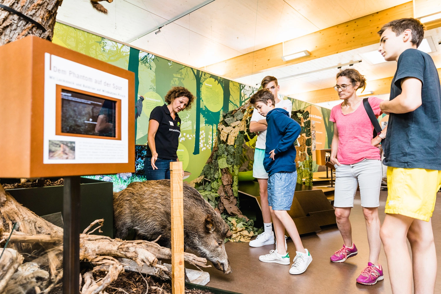Eine Mutter lässt sich mit ihren drei Söhnen von einer Gästeführerin eine Ausstellung über Wildschweine erklären. 