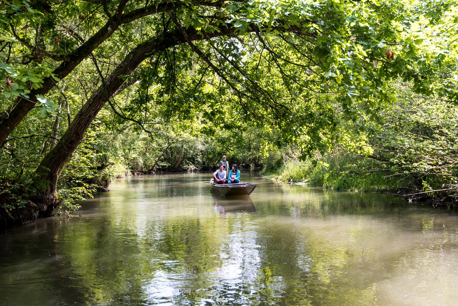 Ein Stocherkahn mit zwei Gästen und einem Fahrer fährt über einen Fluss. 