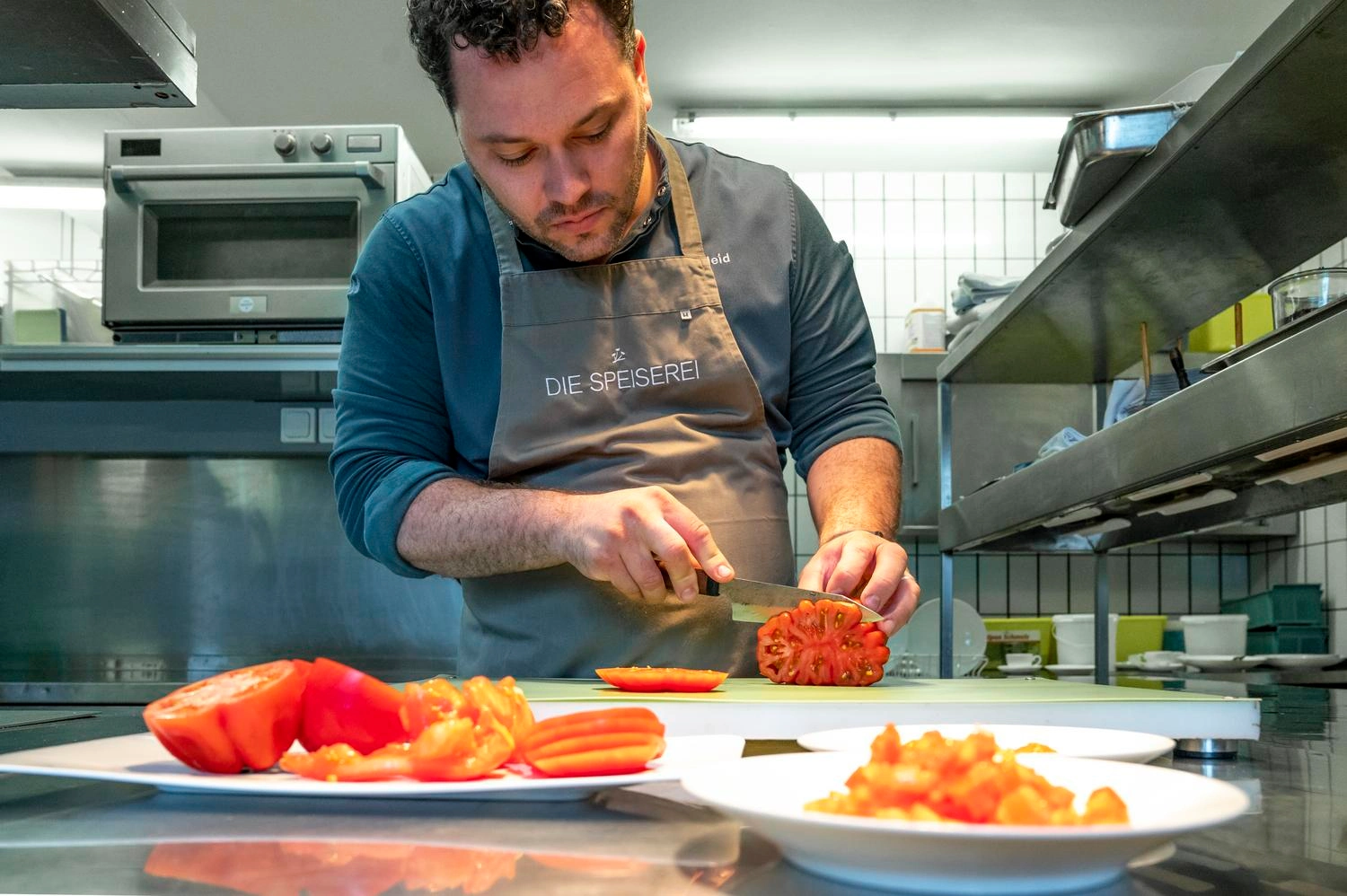 Ein Mann in einer Kochschürze schneidet Tomaten.