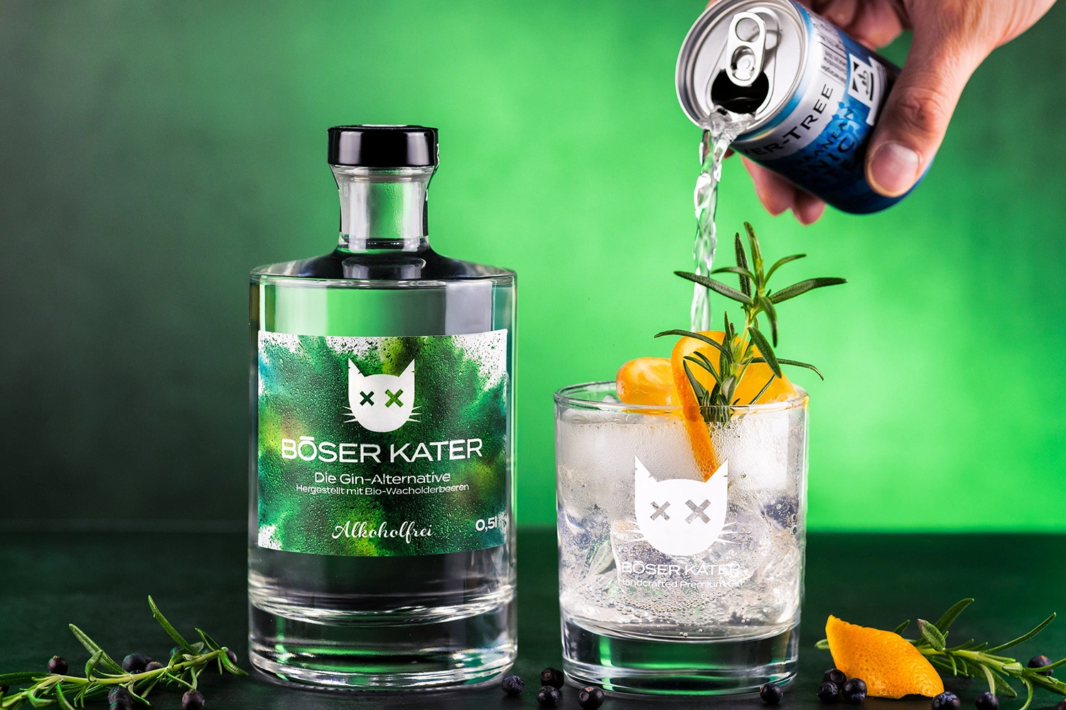 Green non-alcoholic gin bottle with “Böser Kater” printed on it stands next to a glass. The glass is being filled with a can. There is an orange in the glass.
