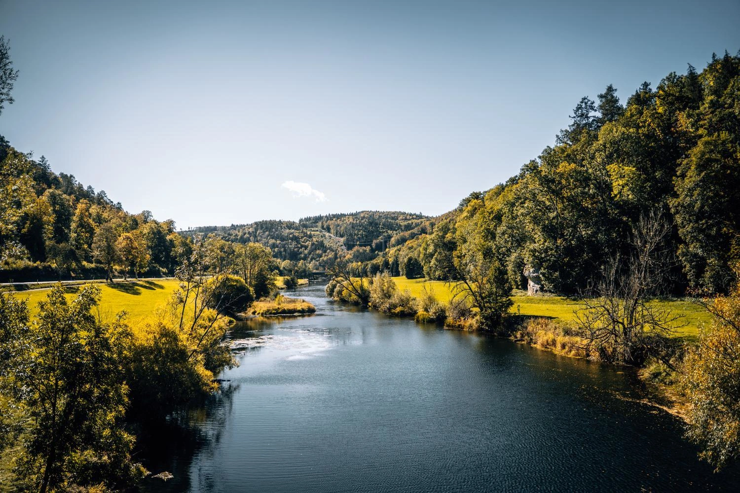 A river landscape with meadows and wooded hills along the Danube under a blue sky.