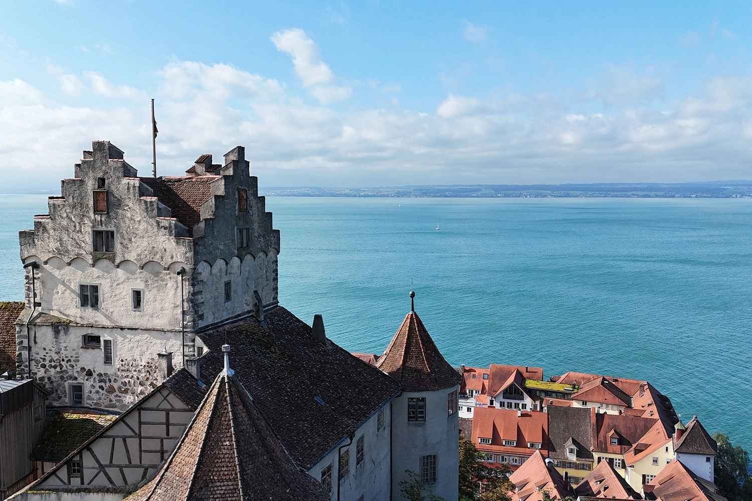 Historische Burg Meersburg mit Staffelgiebeln über roten Dächern, Blick auf den Bodensee; dient als visuelle Einführung zur Region und ihren Sehenswürdigkeiten.