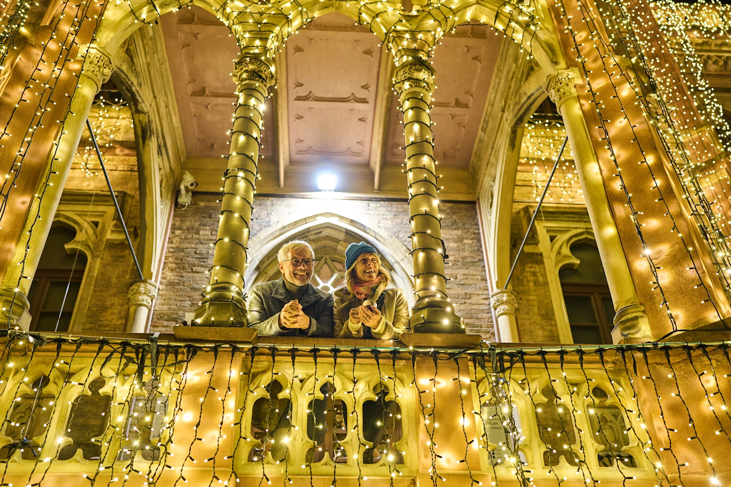 Two people stand in a stone archway decorated all over with fairy lights.