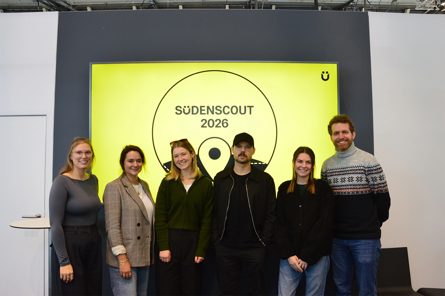 Eine Gruppe von Personen steht vor einer großen gelben „Südenscout 2026“-Anzeige auf einem Messestand.