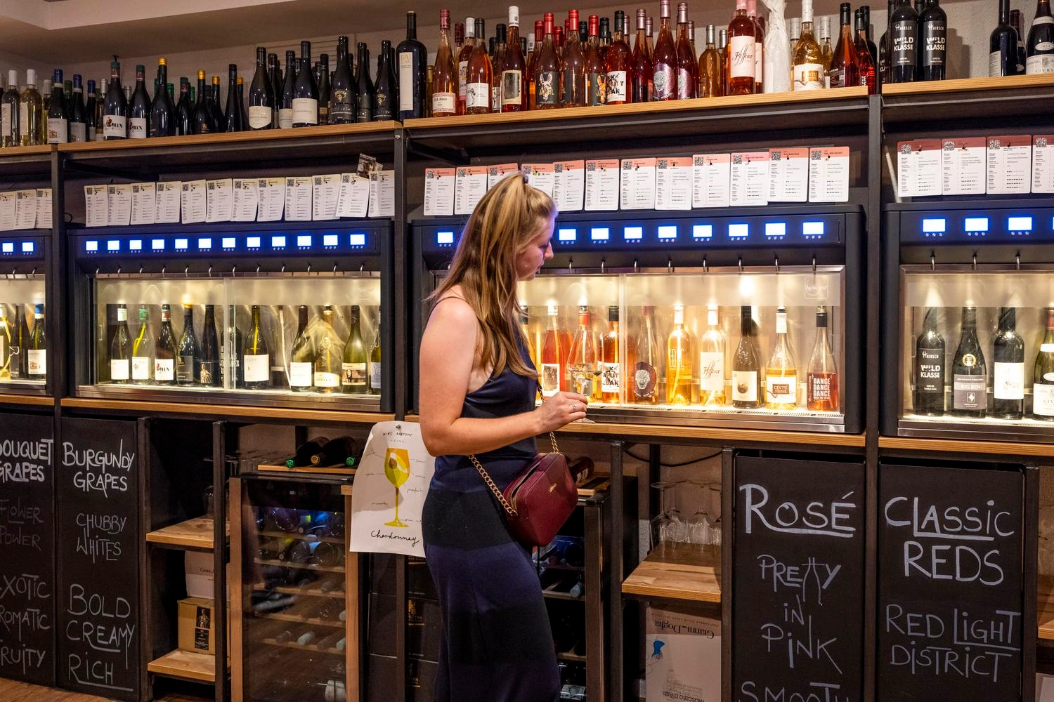 Frau steht in einer Bar vor Schränken, die mit Wein gefüllt sind