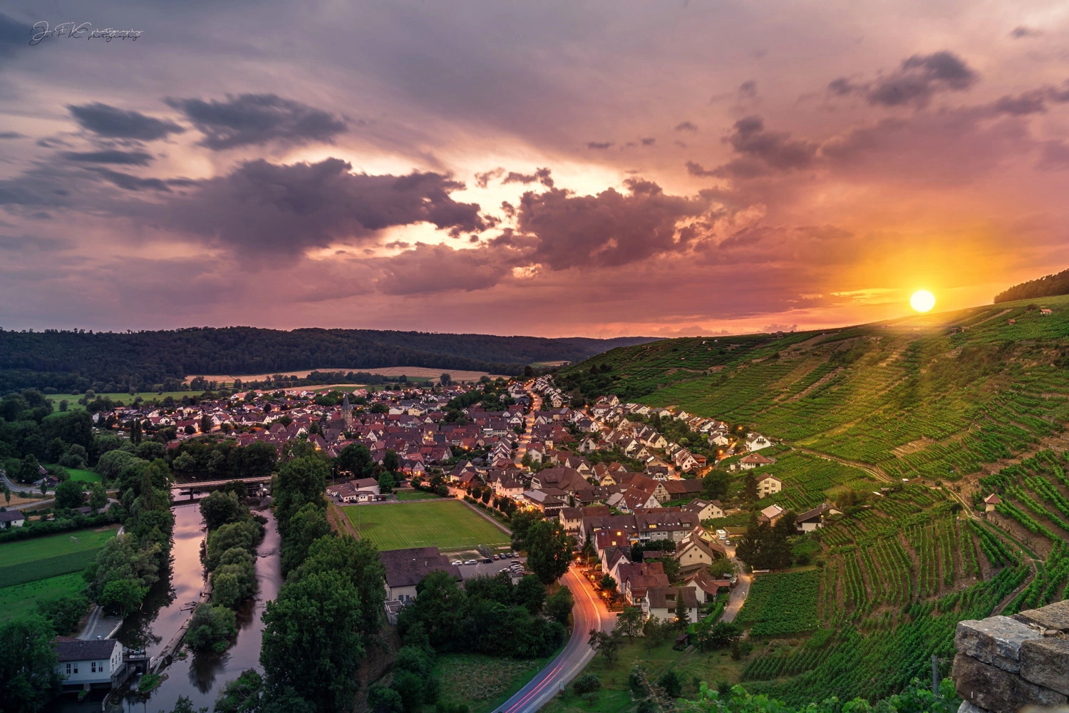 Blick über die Rebhänge Roswanger Halde in der Weinregion Stromberg bei Sonnenuntergang. Im Tal liegt die Ortschaft Vaihingen-Enz an einem Flusslauf. 