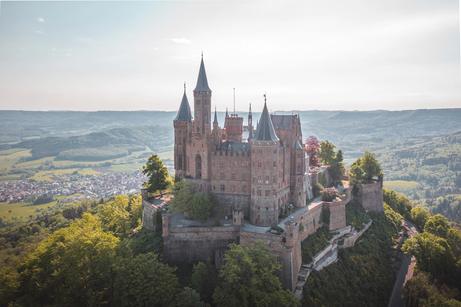 Im Vordergrund ist die Burg Hohenzollern zu sehen, im Hintergrund erstreckt sich die Landschaft der Schwäbischen Alb
