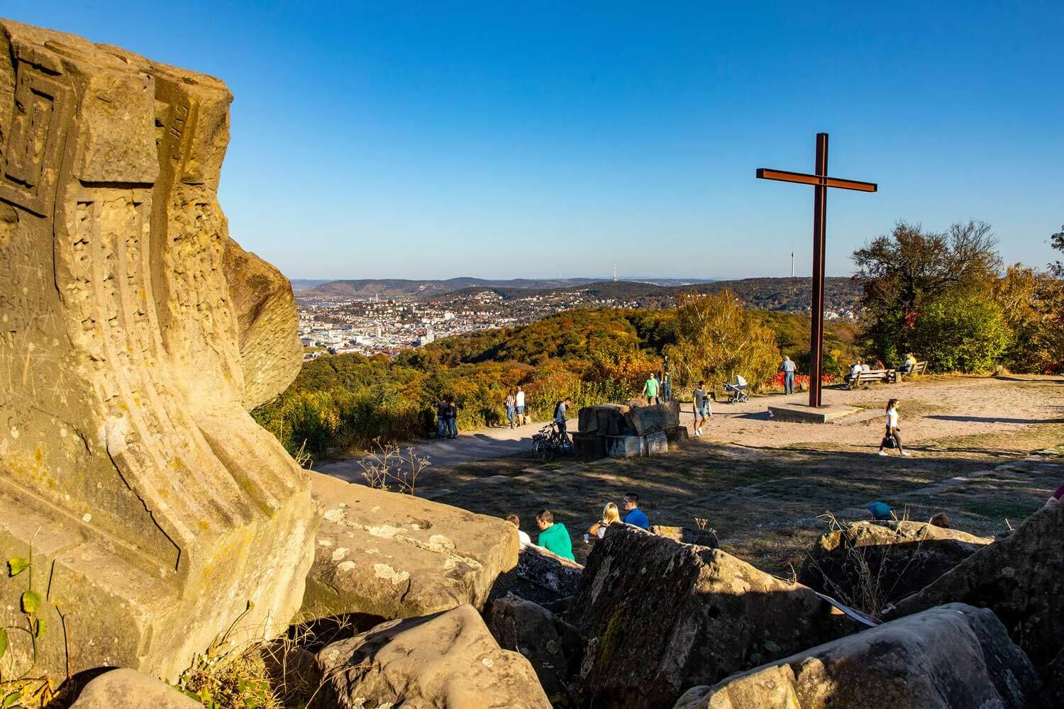 Blick von einem Hügel mit Gipfelkreuz über eine große Stadt