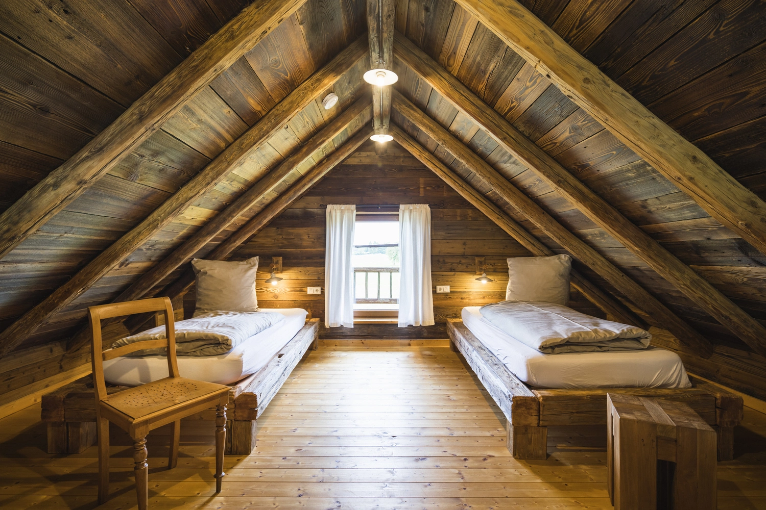 There are two beds in the pitch of the roof of a wooden chalet.