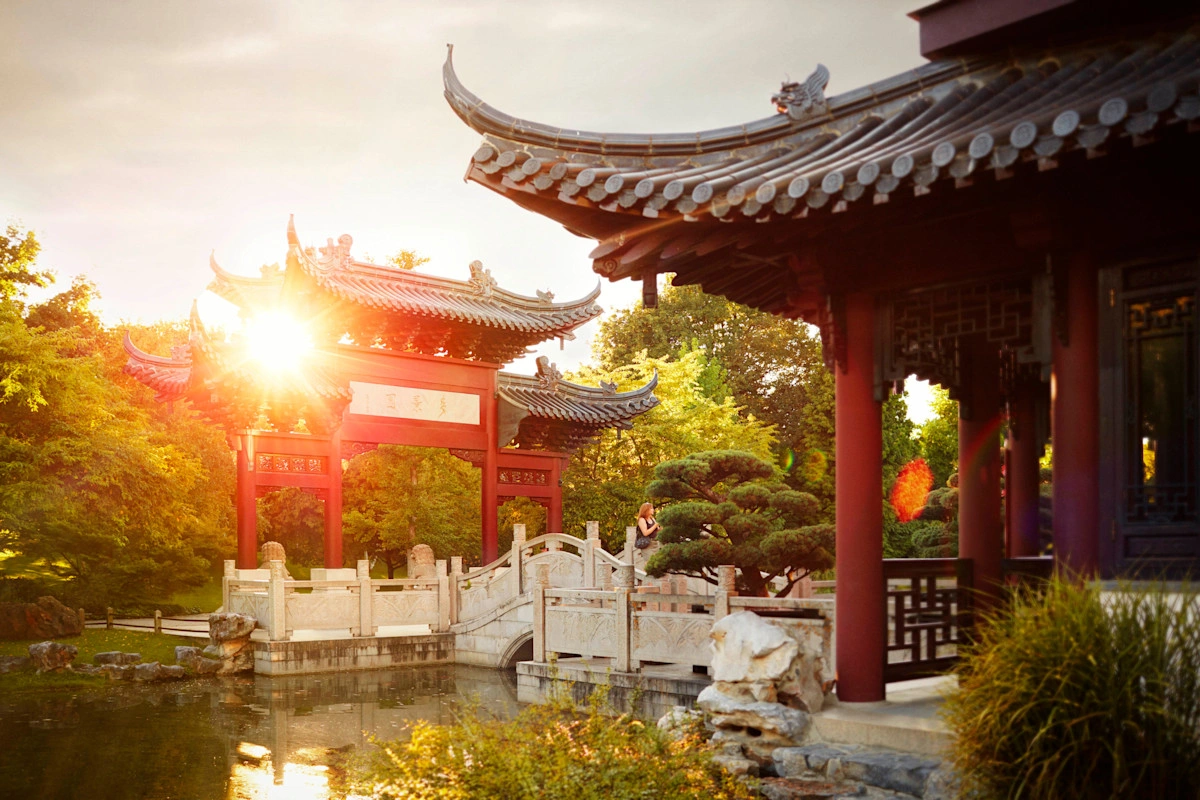 A teahouse and a temple in a Chinese garden. The sun is shining through the temple.