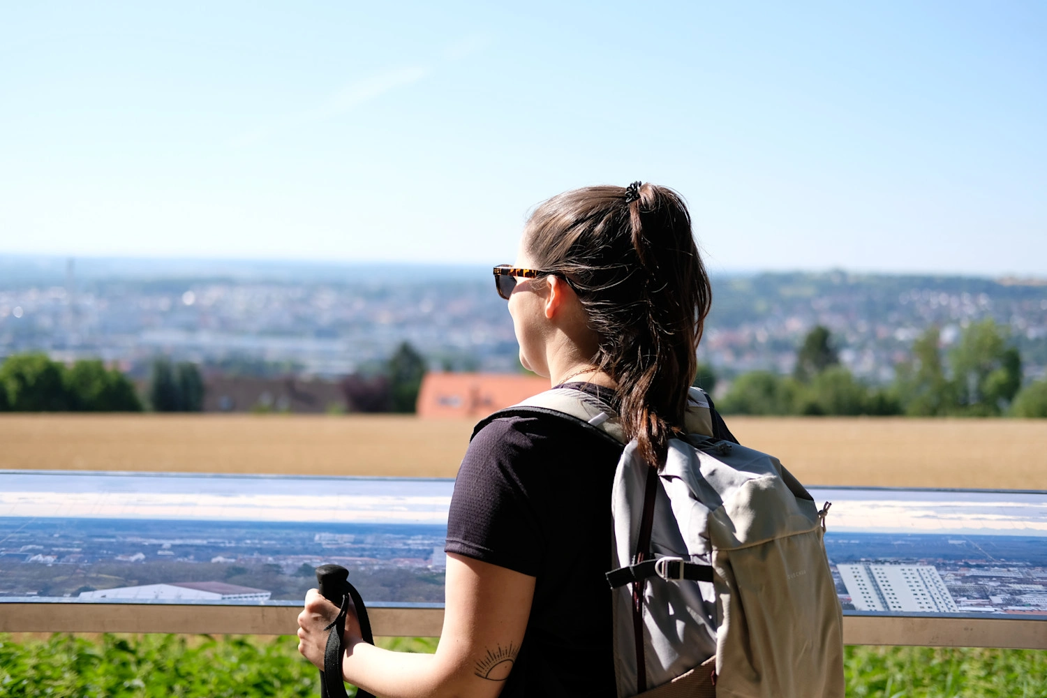 Eine wandernde Frau von hinten mit Wanderrucksack und Wanderstöcken blickt in die Ferne.