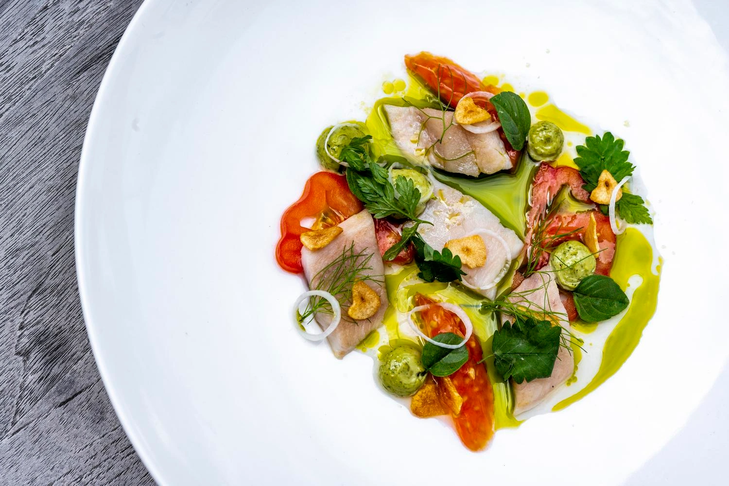 Draufsicht auf einen Teller auf dem Fischstücke, Tomaten und Kräuter angerichtet sind.