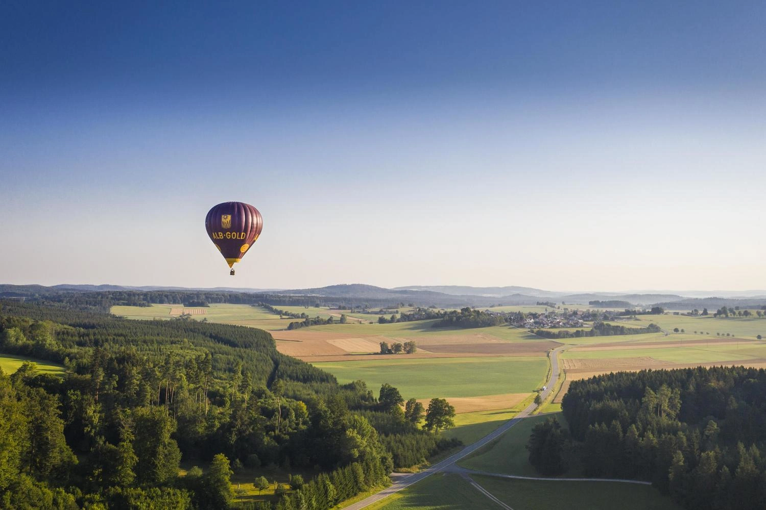 A hot air balloon floats over a hilly landscape.