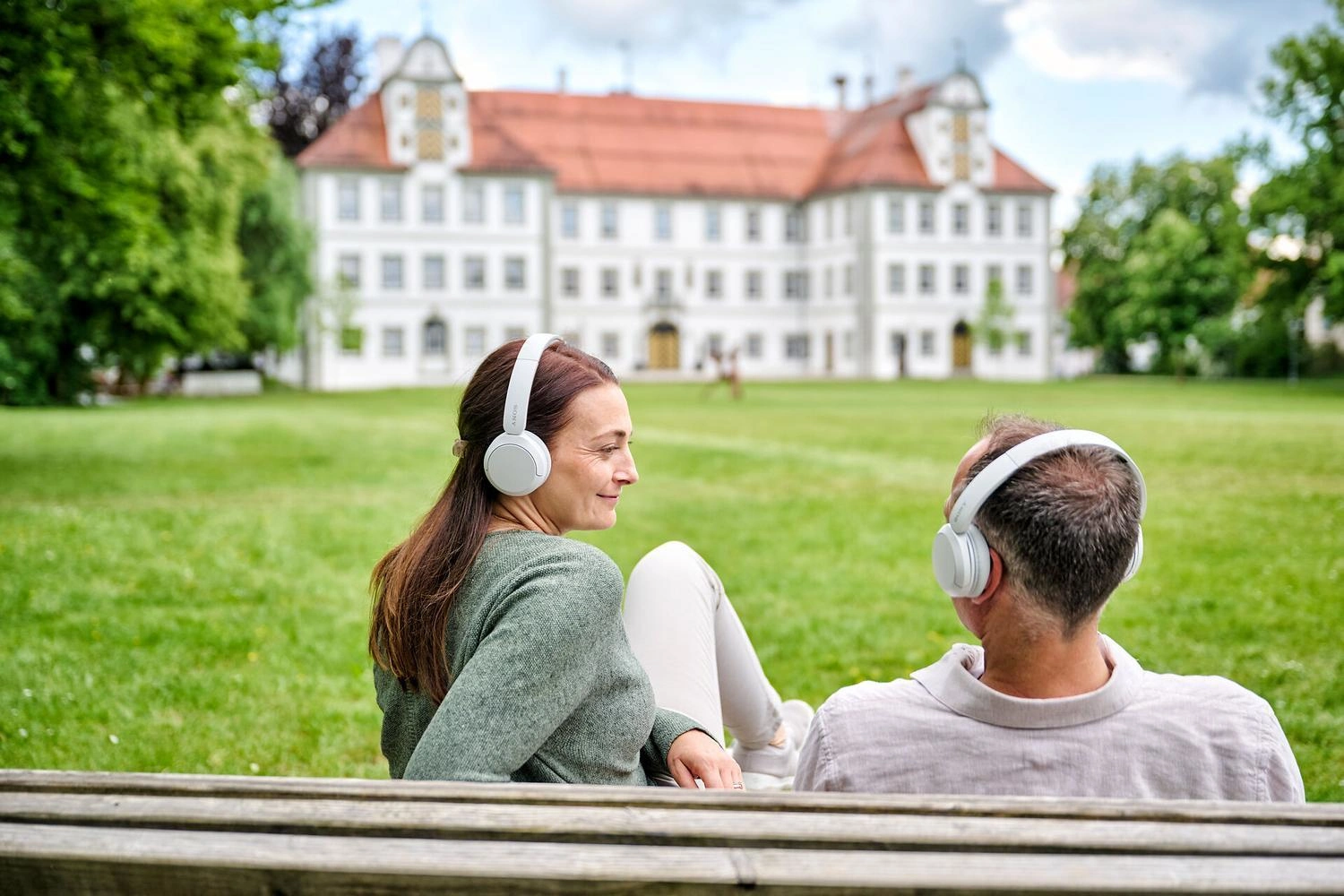Zwei Personen sitzen mit Kopfhörern in einem Schlossgarten.