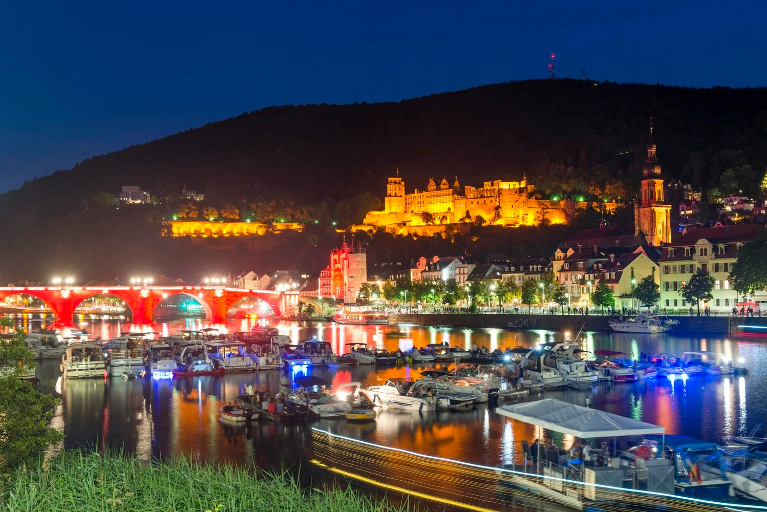 Blick auf eine beleuchtete Stadt am Abend. Im Vordergrund ein Fluss, im Hintergrund ein Schloss.