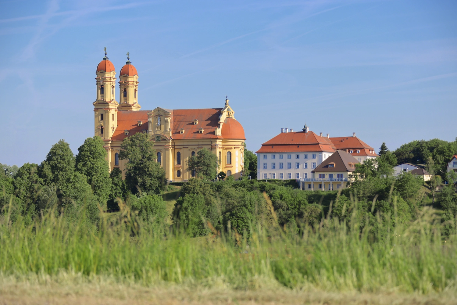 View of a pilgrimage church with outbuildings surrounded by meadows and trees