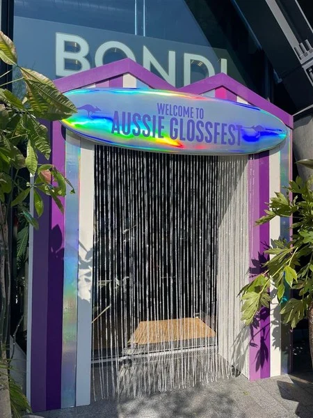 Aussie Gloss Fest entrance with a colourful sign and glossy festival-style booth at Bondi Green